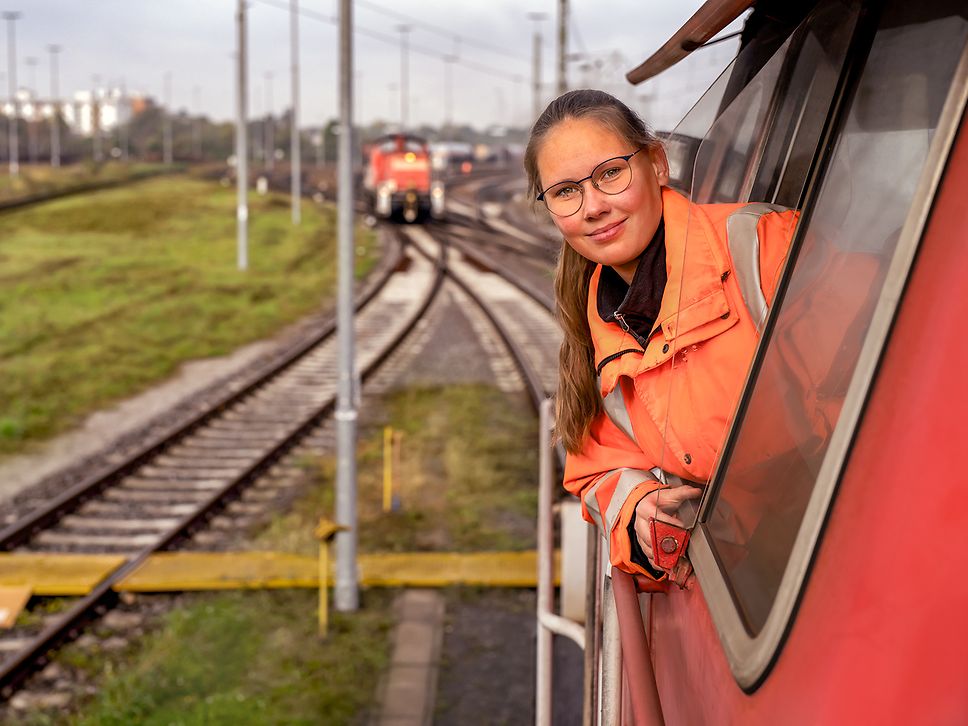 Eine Lokrangierführerin in Warnkleidung sitzt im Führerstand eines Güterzugs und schaut aus dem Fenster