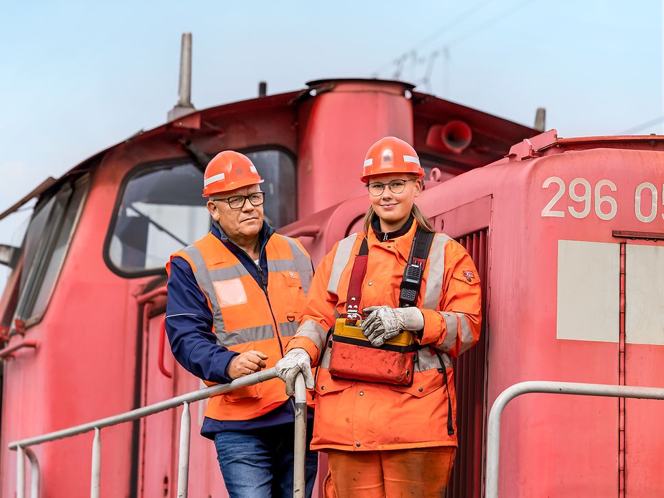 Eine Auszubildende zur Lokführerin steht neben ihrem Ausbilder auf dem Außenpult des Führerstandes eines Güterverkehrszuges