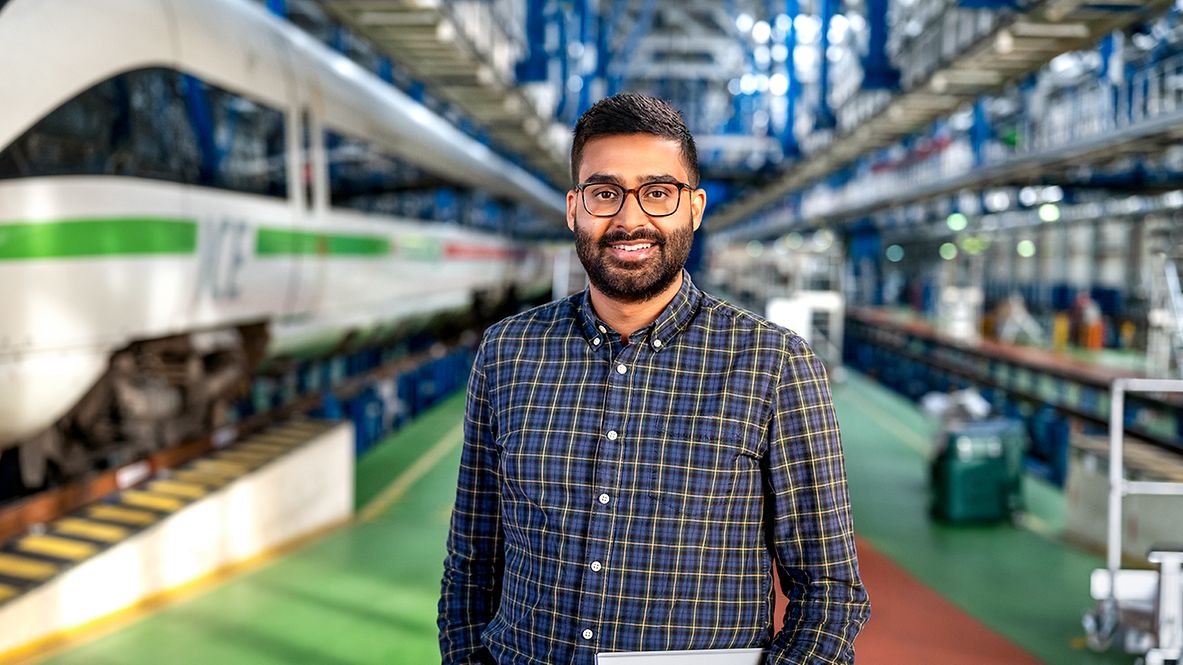Ein Berater steht im ICE-Werk und hält seinen Laptop in der Hand