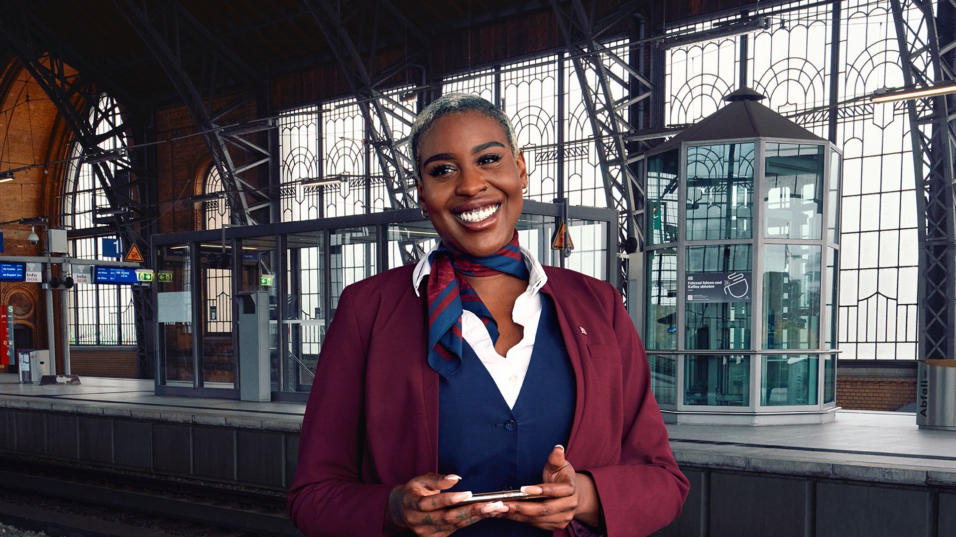 Eine Bordrestaurantleiterin in Unternehmensbekleidung steht am Bahnsteig und hält ein Tablet in der Hand